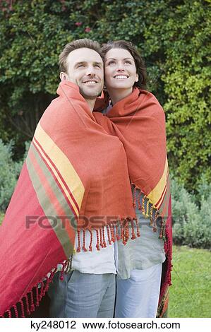Stock Image - Couple wrapped in a shawl and smiling. Fotosearch