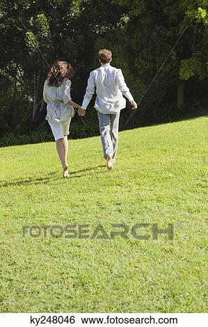Rear view of a couple running on grass View Large Photo Image Stock Photograph - Rear view of a couple running on grass. Fotosearch