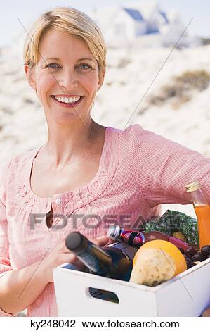 Stock Image - Woman carrying a crate on the beach. Fotosearch
