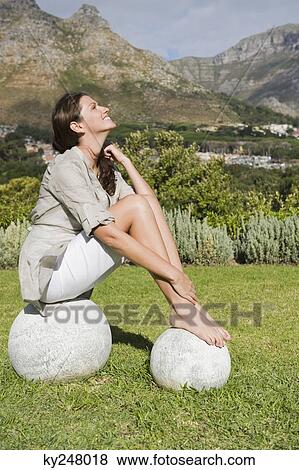 Stock Photo - Woman sitting on round stones and smiling. Fotosearch