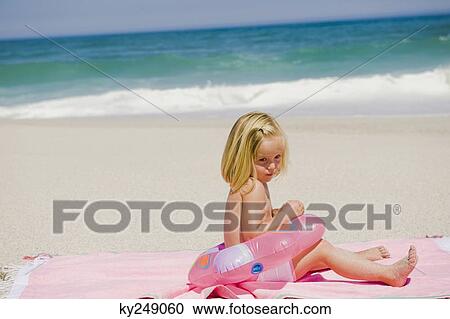 Stock Image - Girl sitting with an inflatable ring on the beach. Fotosearch