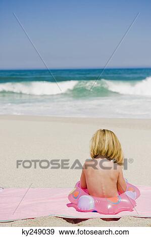 Stock Photo - Girl sitting with an inflatable ring on the beach. Fotosearch