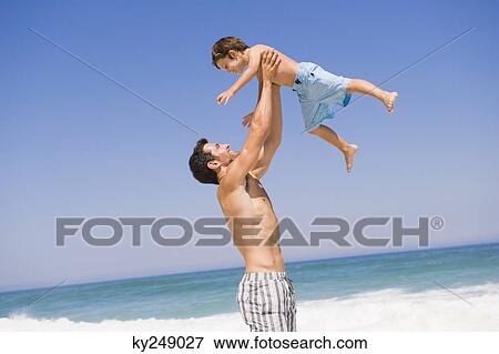 Stock Photo - Man playing with his son on the beach. Fotosearch