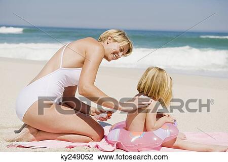 Stock Image - Woman applying suntan lotion on her daughter on the beach. Fotosearch
