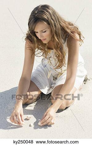 Stock Photo - Woman playing with seashells on the beach. Fotosearch