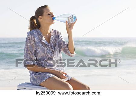 Woman sitting on an ice box and drinking water on the beach View Large Photo Image Stock Photo - Woman sitting on an ice box and drinking water on the beach. Fotosearch