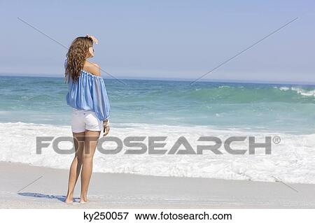 Woman standing on the beach and looking at a view View Large Photo Image Stock Photo - Woman standing on the beach and looking at a view. Fotosearch