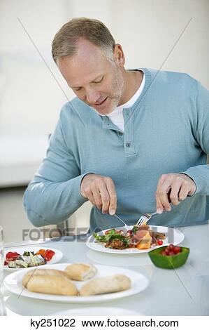 Stock Image - Man having breakfast at a dining table. Fotosearch