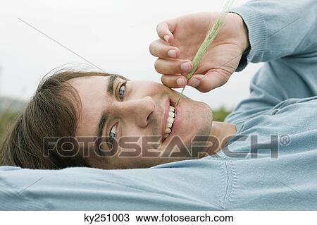 Stock Image - Portrait of a man biting a stalk of wheat. Fotosearch