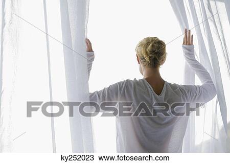 Stock Image - Rear view of a woman opening the curtain of balcony. Fotosearch