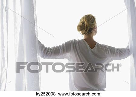 Rear view of a woman opening the curtain of balcony View Large Photo Image Stock Photo - Rear view of a woman opening the curtain of balcony. Fotosearch