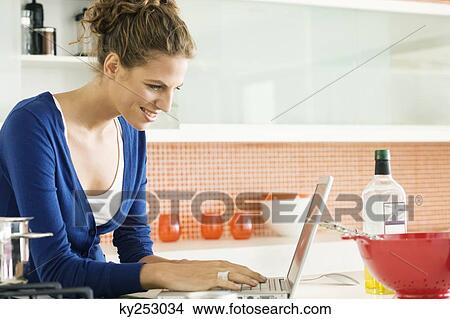 Woman reading a recipe on a laptop in the kitchen View Large Photo Image Picture - Woman reading a recipe on a laptop in the kitchen. Fotosearch