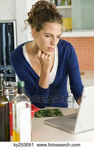 Woman reading a recipe on a laptop in the kitchen View Large Photo Image Stock Image - Woman reading a recipe on a laptop in the kitchen. Fotosearch