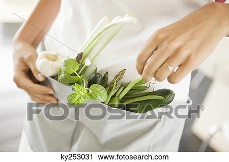 Stock Image - Woman standing with vegetables in the kitchen. Fotosearch