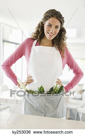 Stock Photograph - Woman standing with vegetables in the kitchen. Fotosearch