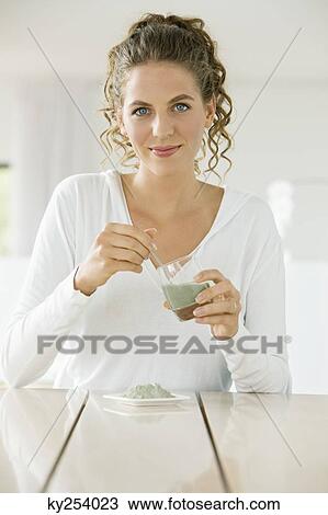 Stock Image - Portrait of a woman mixing green clay for facial mask. Fotosearch