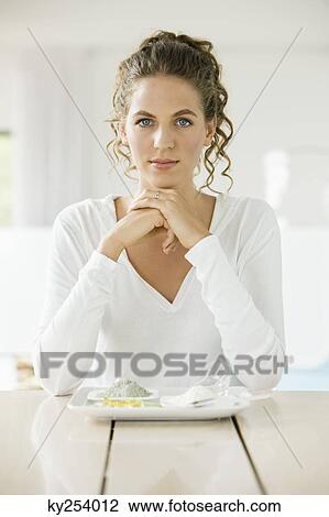 Stock Image - Portrait of a woman sitting at a table with clays on a plate. Fotosearch