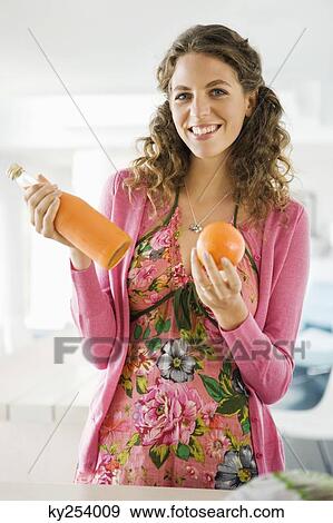 Woman holding orange juice with an orange in the kitchen View Large Photo Image Stock Photo - Woman holding orange juice with an orange in the kitchen. Fotosearch