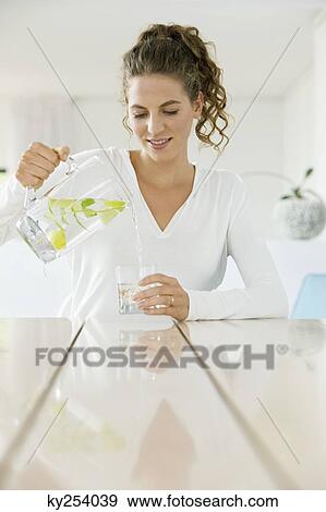 Stock Photo - Woman pouring lemonade into a glass from a jug. Fotosearch