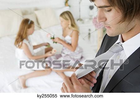 Groom adjusting his tie with two girls in the background View Large Photo Image Stock Photography - Groom adjusting his tie with two girls in the background. Fotosearch