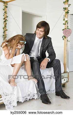 Groom consoling a desperate girl sitting on the bed covering her face View Large Photo Image Stock Photograph - Groom consoling a desperate girl sitting on the bed covering her face. Fotosearch