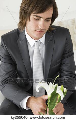 Groom sitting on the bed and holding a lily flower View Large Photo Image Stock Image - Groom sitting on the bed and holding a lily flower. Fotosearch