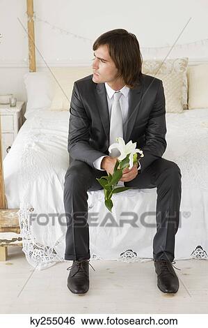 Groom sitting on the bed and holding a lily flower View Large Photo Image Stock Photograph - Groom sitting on the bed and holding a lily flower. Fotosearch