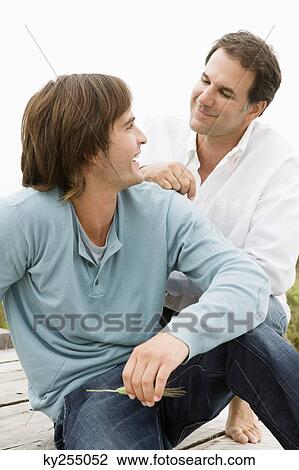 Stock Image - Two men sitting on a boardwalk. Fotosearch