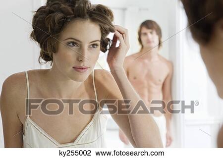 Stock Image - Woman using curlers with her boyfriend in the background. Fotosearch