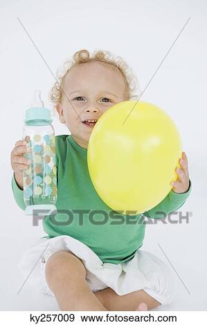Stock Photo - Baby boy holding a balloon and a baby bottle. Fotosearch