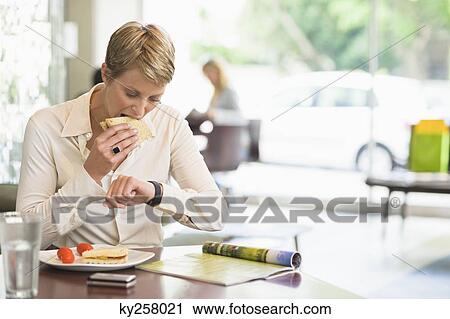 Businesswoman eating in a restaurant and checking the time View Large Photo Image Stock Image - Businesswoman eating in a restaurant and checking the time. Fotosearch