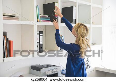 Businesswoman putting a ring binder in a shelf View Large Photo Image Picture - Businesswoman putting a ring binder in a shelf. Fotosearch