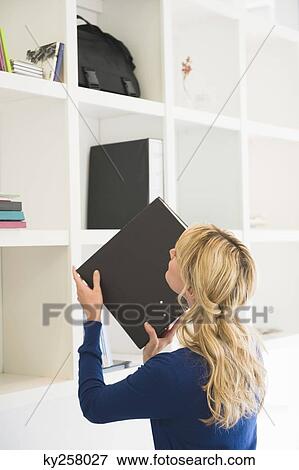 Stock Photo - Businesswoman putting a ring binder in a shelf. Fotosearch
