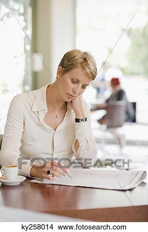Businesswoman sitting in a restaurant and reading a financial newspaper View Large Photo Image Picture - Businesswoman sitting in a restaurant and reading a financial newspaper. Fotosearch