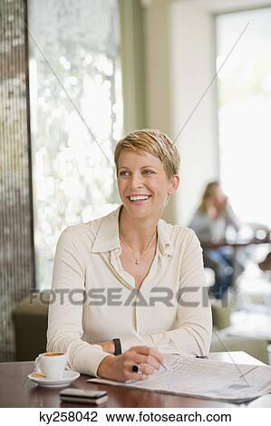 Stock Image - Businesswoman sitting in a restaurant and reading a financial newspaper. Fotosearch