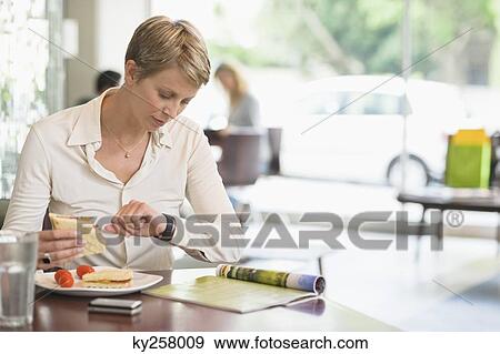 Stock Photo - Businesswoman sitting in a restaurant and checking the time. Fotosearch