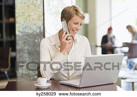 Businesswoman talking on a mobile phone and looking at a laptop View Large Photo Image Stock Photo - Businesswoman talking on a mobile phone and looking at a laptop. Fotosearch