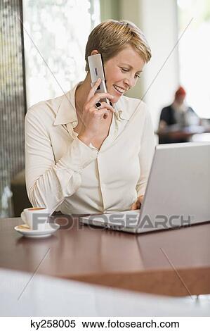 Businesswoman talking on a mobile phone and looking at a laptop View Large Photo Image Stock Photography - Businesswoman talking on a mobile phone and looking at a laptop. Fotosearch