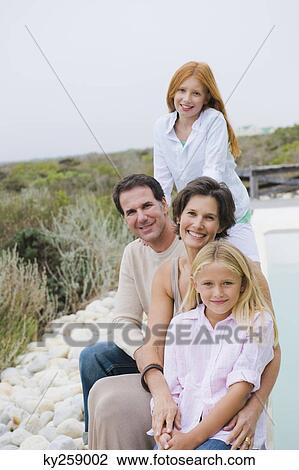 Stock Image - Family sitting at the poolside. Fotosearch