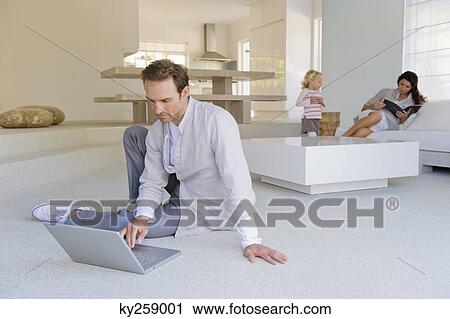 Stock Image - Man working on a laptop with his family in the background. Fotosearch