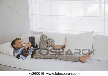 Boy lying on a couch and reading a book View Large Photo Image Stock Photograph - Boy lying on a couch and reading a book. Fotosearch