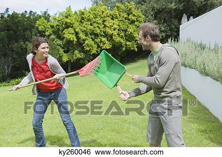 Couple playing with gardening equipments in a lawn View Large Photo Image Stock Photograph - Couple playing with gardening equipments in a lawn. Fotosearch