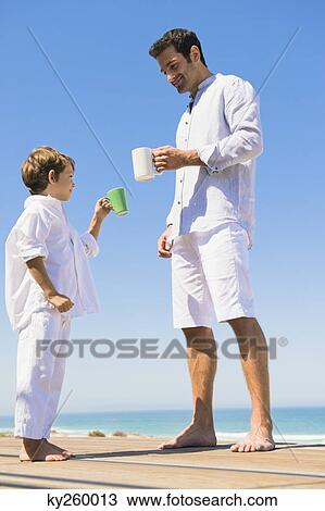 Man and his son holding coffee cups on the beach View Large Photo Image Stock Image - Man and his son holding coffee cups on the beach. Fotosearch