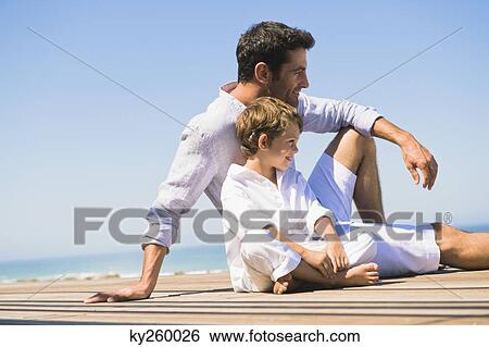 Man sitting on a boardwalk with his son View Large Photo Image Stock Photograph - Man sitting on a boardwalk with his son. Fotosearch