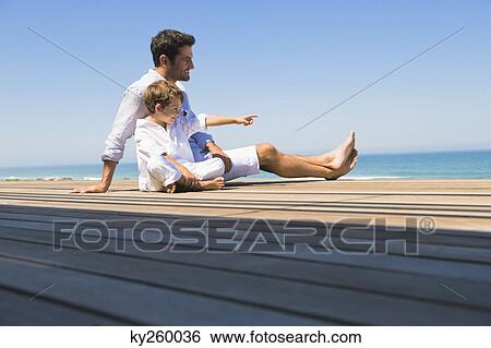 Man sitting on a boardwalk with his son View Large Photo Image Stock Photograph - Man sitting on a boardwalk with his son. Fotosearch