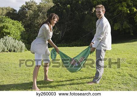 Stock Image - Parents swinging their daughter in a lawn. Fotosearch