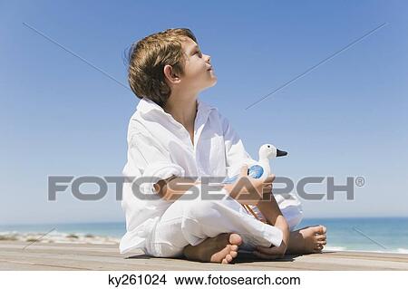 Boy sitting on a boardwalk and holding a toy bird View Large Photo Image Picture - Boy sitting on a boardwalk and holding a toy bird. Fotosearch