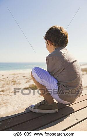 Boy sitting on a boardwalk View Large Photo Image Stock Photo - Boy sitting on a boardwalk. Fotosearch