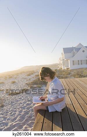 Girl sitting on a boardwalk and reading a book View Large Photo Image Picture - Girl sitting on a boardwalk and reading a book. Fotosearch