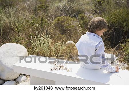 Rear view of a boy sitting on a concrete bench View Large Photo Image Stock Image - Rear view of a boy sitting on a concrete bench. Fotosearch